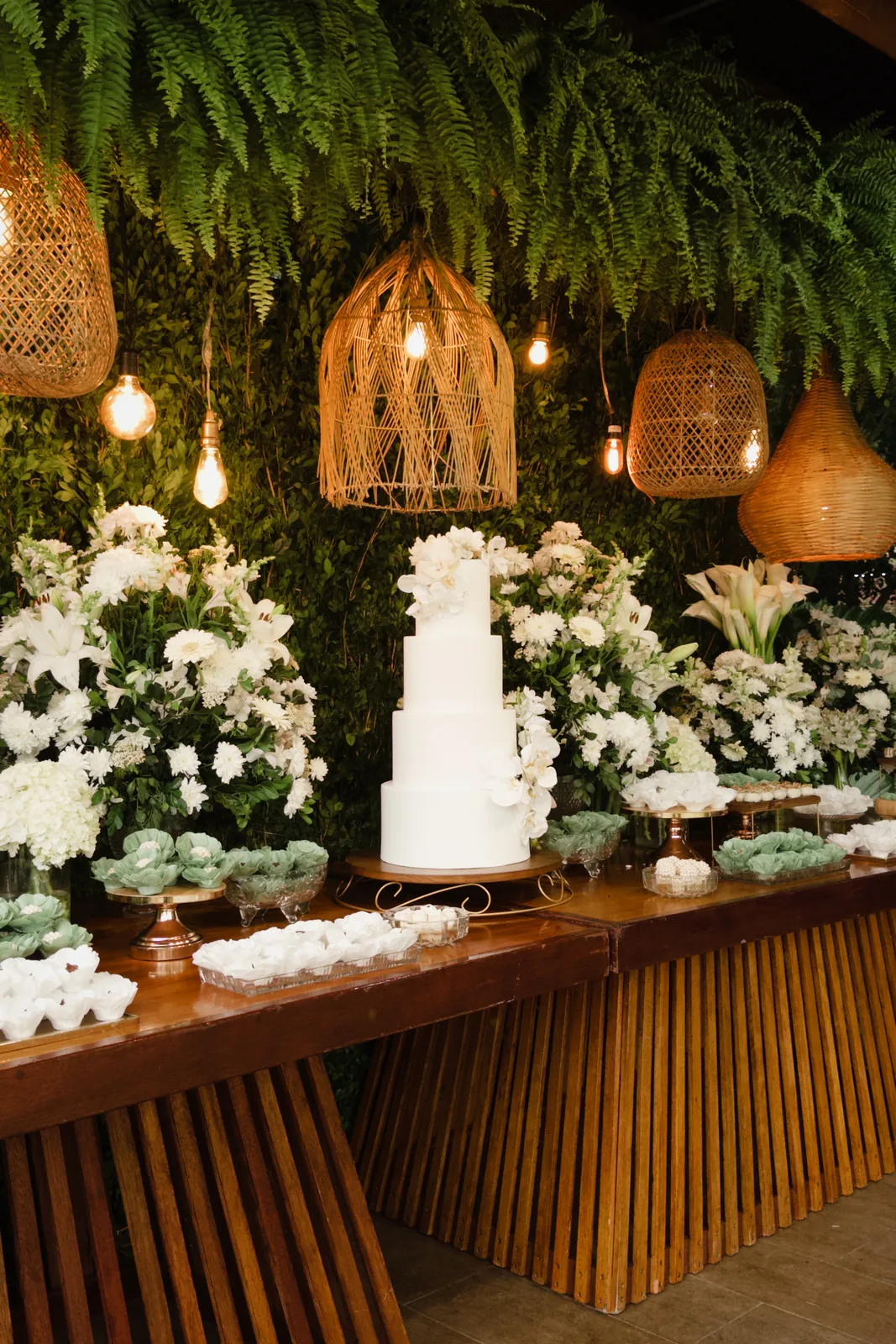 Mesa do bolo com flores brancas e folhagens no casamento
